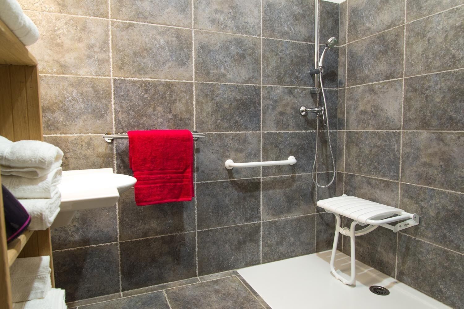 Een badkamer met een douche, een wit wastafel en een rode handdoek op een rek.