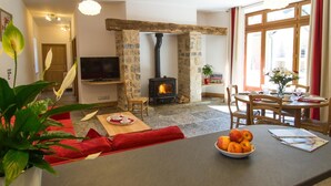 Ein gemütliches Wohnzimmer mit Kamin aus Stein, einem Fernseher und einer Essecke mit Tisch für zwei Personen.