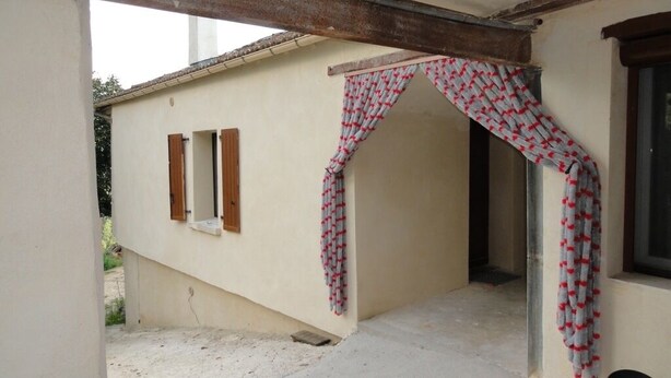 Un espacio al aire libre cubierto, con piso de concreto, techo de vigas de madera y cortina estampada.