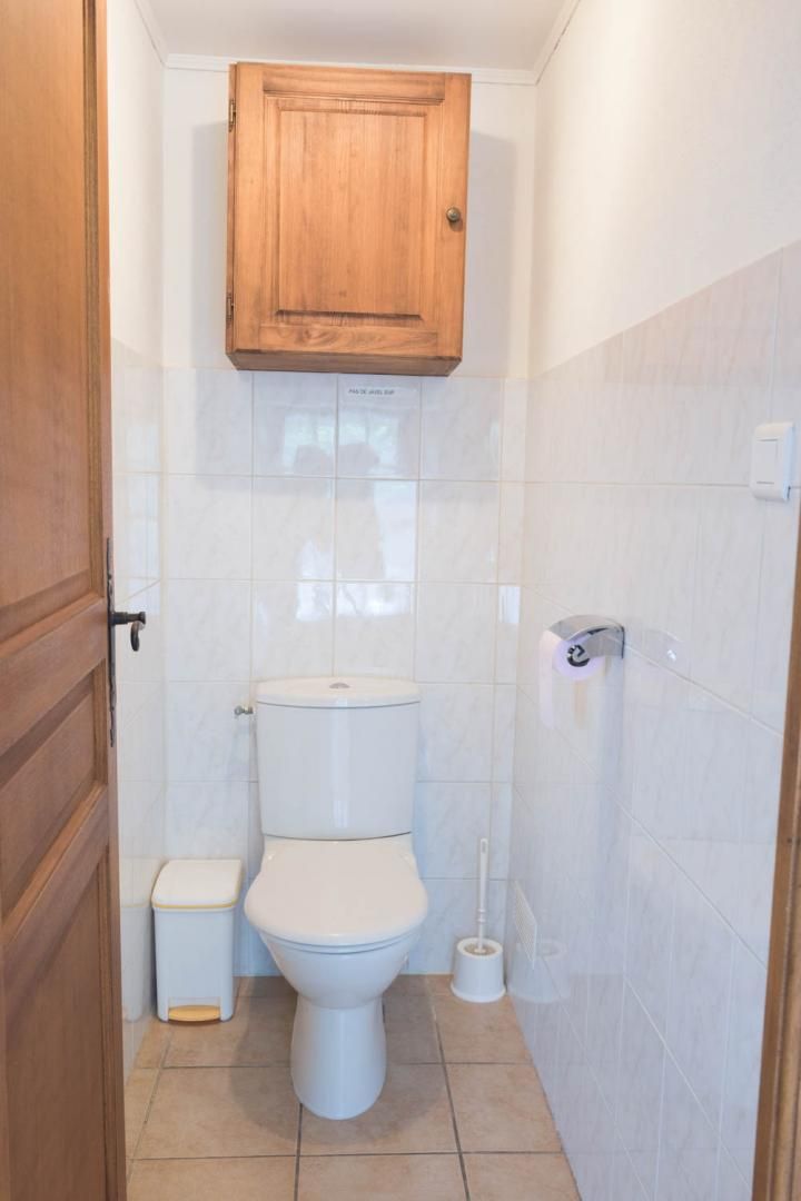 Et lille badeværelse med toilet, et træskab over toilettet og toiletpapirholder på væggen.