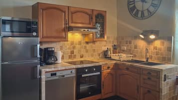 Una cucina con mobili in legno, un frigorifero in acciaio inossidabile, un forno a microonde, una lavastoviglie, un forno e un lavello, oltre a un orologio a parete di grandi dimensioni.