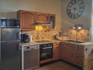 Una cucina con mobili in legno, un frigorifero in acciaio inossidabile, un forno a microonde, una lavastoviglie, un forno e un lavello, oltre a un orologio a parete di grandi dimensioni.