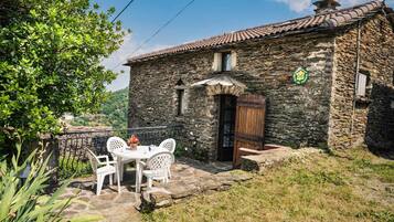 Un edificio in pietra con tetto in tegole, una porta in legno e una piccola finestra. C'è un tavolo con sedie all'esterno.