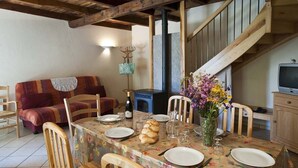 A dining area with a wooden table set for four, surrounded by wooden chairs. A vase with flowers is on the table, and there is a blue cabinet to the right.