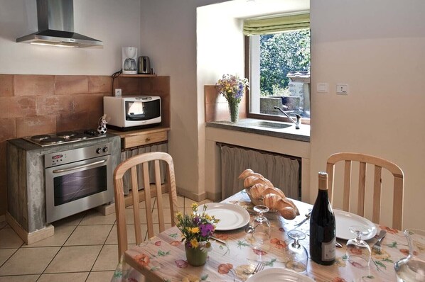 A compact kitchen with a stove, microwave, and a dining table set for two with a bottle of wine and a vase of flowers.
