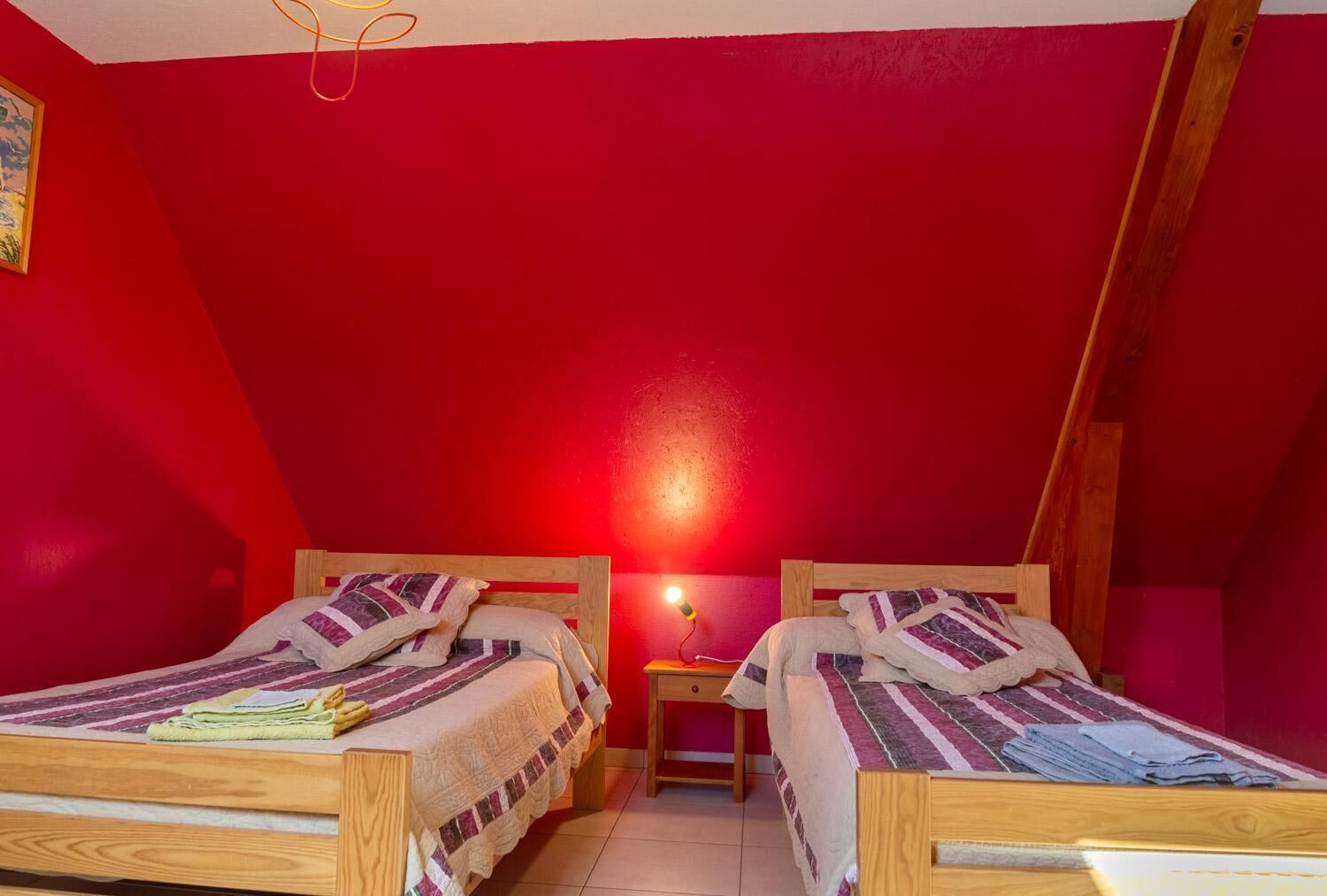 Una habitación pequeña con paredes rojas, dos camas de madera, una mesita de noche y una lámpara en cada cama.