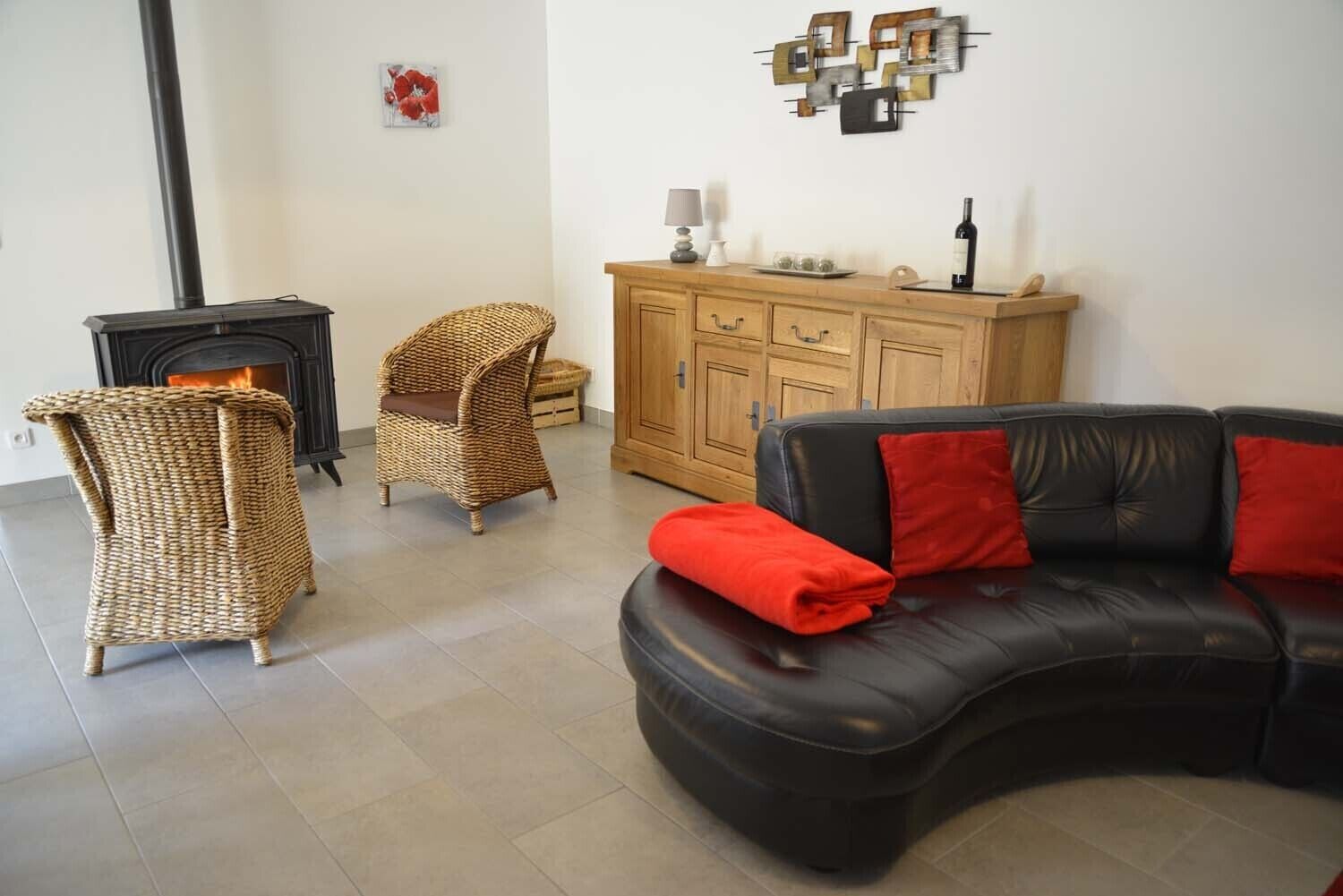 A living room with a black leather sofa, two wicker chairs, a wooden cabinet, and a fireplace.