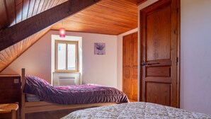 A bedroom with a sloped ceiling, a window, a door, and a bed.