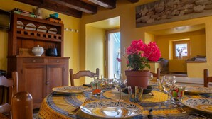 A dining area with a table set for four, surrounded by wooden chairs. A potted plant with pink flowers is on the table.