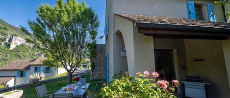A house with a patio, a dining table with chairs, and a garden with flowers.