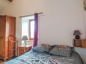 A bedroom with a bed, a wooden wardrobe, a bedside table with a lamp, and a window with a curtain.