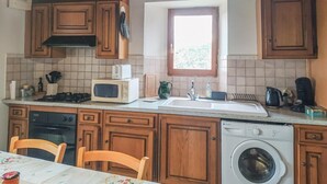 A kitchen with wooden cabinets, a microwave, a stove, a sink, a window, and a washing machine.
