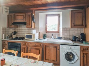 A kitchen with wooden cabinets, a microwave, a stove, a sink, a window, and a washing machine.