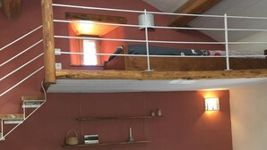 Et loftrum med en trappe i træ, køjeseng og spiseplads med to stole og et bord.