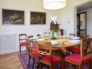 A dining room with a round table set for six, surrounded by wooden chairs with red cushions. There are two paintings on the wall above the table, a radiator below, and a patterned rug on the floor. - Enjoy Panoramic Views Of Florence From Your Rooftop Terrace (Florenz)