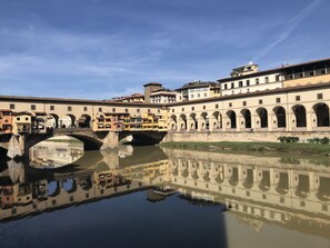 A historic bridge with arches reflecting in the water, surrounded by buildings with multiple stories and balconies. - Enjoy Panoramic Views Of Florence From Your Rooftop Terrace  (Florenz)