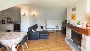 A cozy living room with a fireplace, a dining area with a table and chairs, and a kitchen area with a coffee machine.