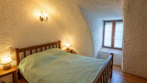 A cozy bedroom with a sloped ceiling, a wooden bed, a bedside lamp, and a window with curtains.