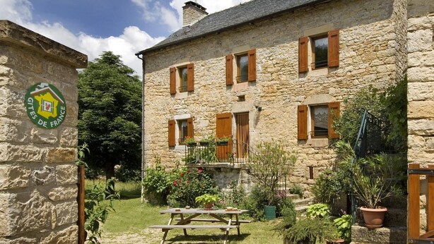 Un edificio de piedra con un patio, contraventanas de madera y una mesa de picnic.