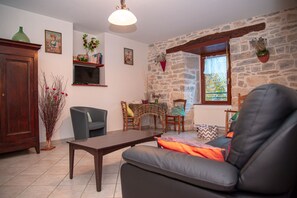 A cozy living room with a stone wall, a wooden cabinet, a television, a sofa, and a dining table with chairs.
