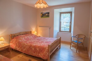 A bedroom with a wooden bed, a chair, a radiator, a window, and a picture on the wall.