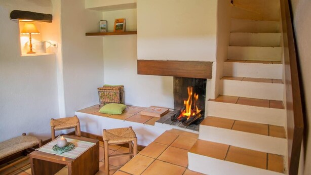 Una habitación acogedora con chimenea, una escalera y una zona de estar con una mesa y sillas.