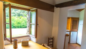 Una habitación con una mesa de madera, una silla, un ventanal con vistas a la vegetación y una puerta que da a otra habitación.
