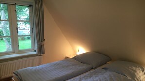 Une chambre avec deux lits simples, une fenêtre avec des rideaux, un radiateur et une lampe fixée au mur.