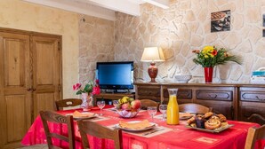 A dining area with a stone wall, wooden furniture, a television, and a table set with food and drinks.