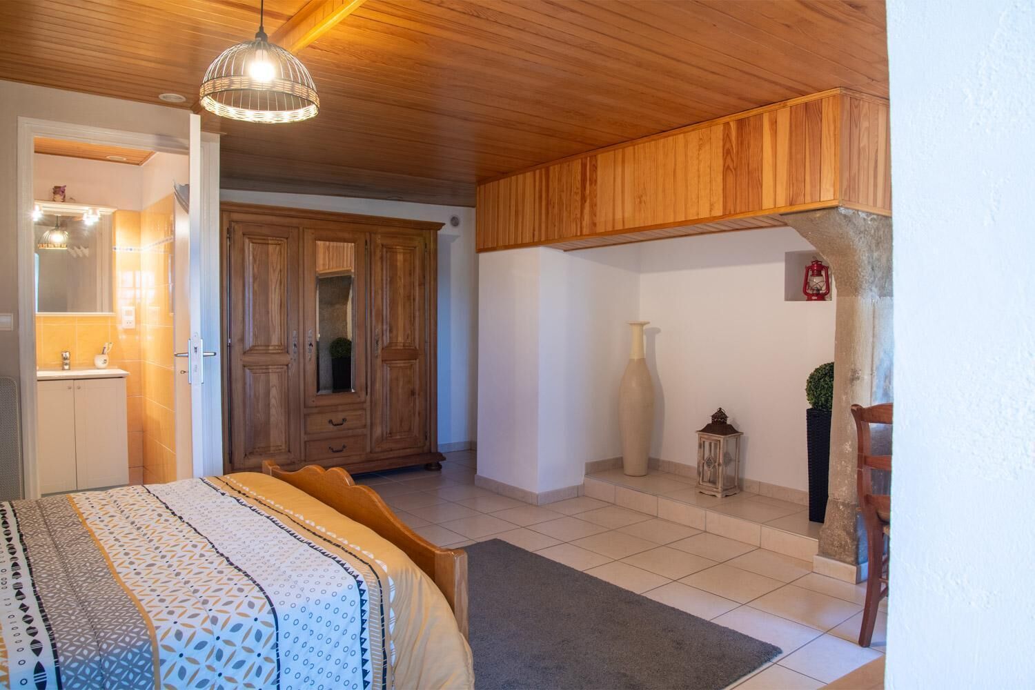 A bedroom with a bed, wooden wardrobe, and a hanging light fixture.