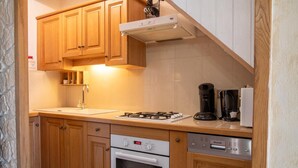 A compact kitchen with wooden cabinets, a gas stove, a built-in oven, a coffee maker, and a dishwasher.