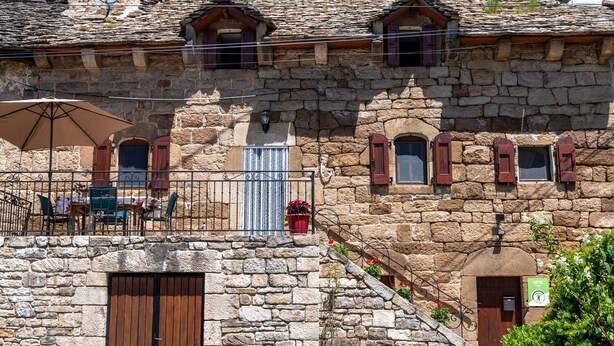 A stone building with a balcony, a wooden door, and a small window with shutters.