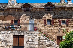 Un bâtiment en pierre doté d’un balcon, d’une porte en bois et d’une petite fenêtre avec des volets.