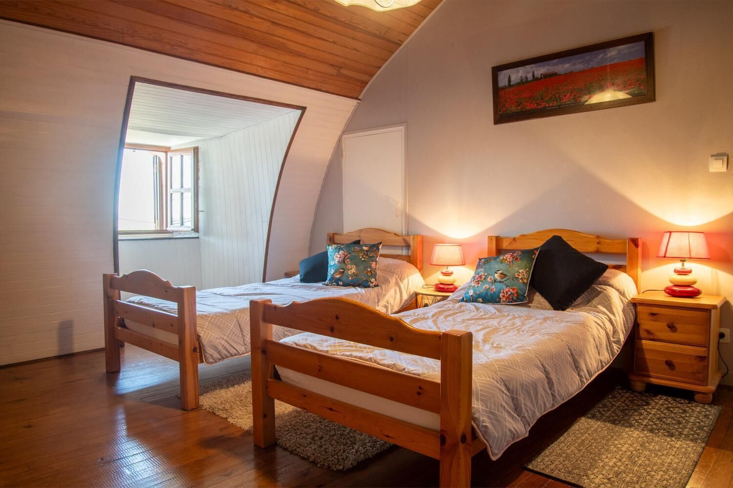 Un dormitorio acogedor con dos camas de madera, una silla de madera, una mesita y un cuadro en la pared.