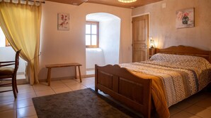 A bedroom with a wooden bed, a bench, a small table, and a window with curtains.