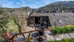Un edificio de techo de piedra con un pequeño patio, una reja metálica y vistas a un paisaje montañoso.