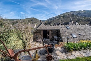 A stone-roofed building with a small patio, a metal gate, and a view of a hilly landscape.