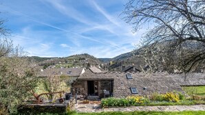 Una cabaña de piedra con jardín, un pequeño espacio de estar al aire libre y vistas del pueblo circundante.