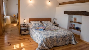Une chambre avec un lit en bois, deux lampes de chevet, un jeu de société Monopoly et une bibliothèque contenant des livres et un bol bleu.