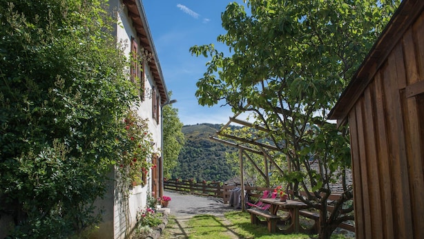 Une cour avec une table et des chaises en bois, entourée de verdure et offrant une vue sur une colline.