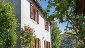 Un bâtiment rustique à la façade blanche, doté de volets en bois et d’un escalier en pierre menant à l’entrée.