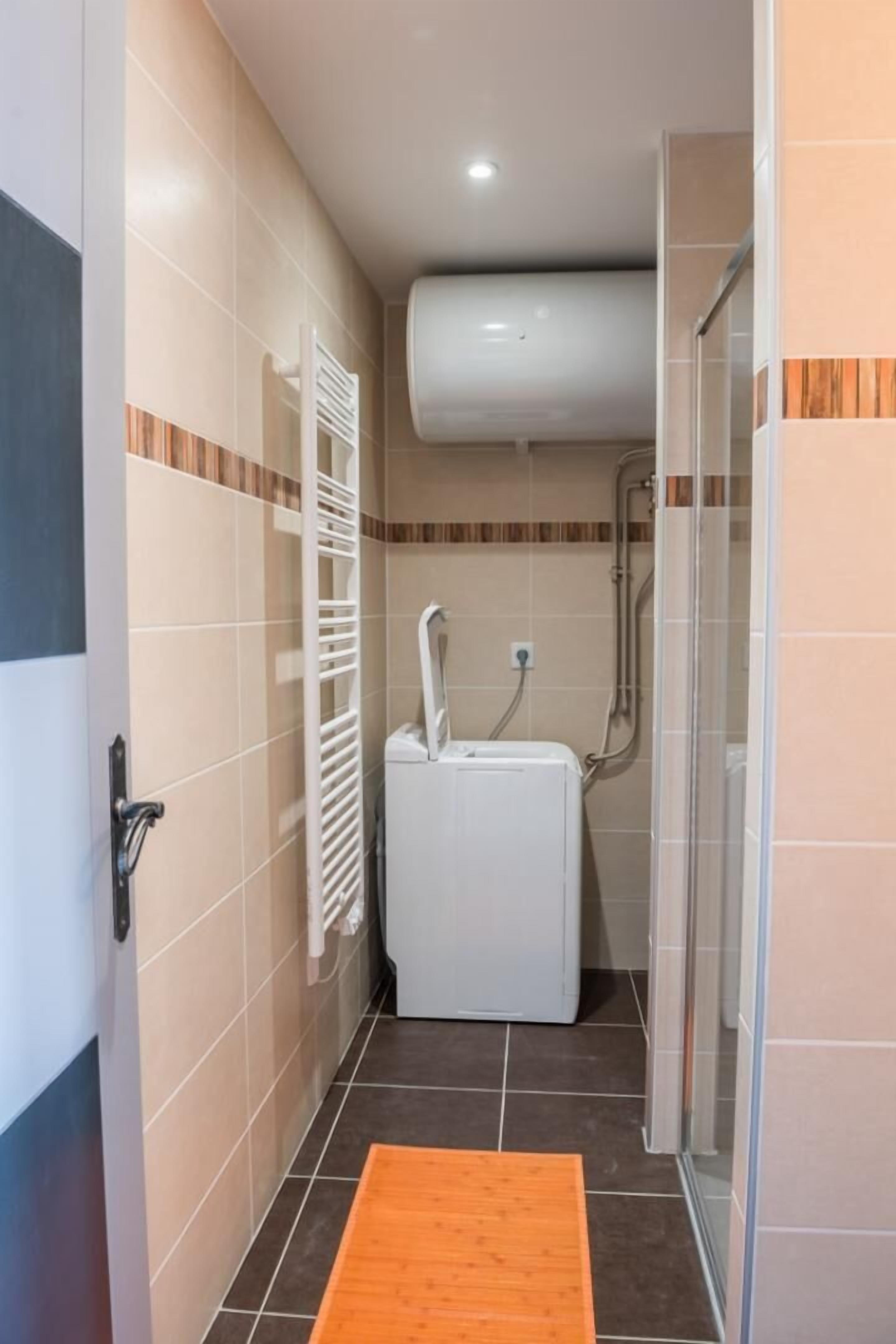 Un baño pequeño con un radiador blanco, una lavadora blanca y zona de ducha.