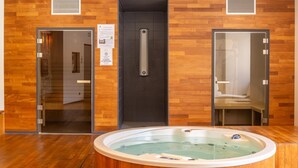 Un cuarto de spa con pared de madera, puerta de cristal, bañera de hidromasaje y zona de ducha.