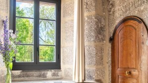 Una habitación con paredes de piedra, una puerta de madera, una ventana con contraventanas negras y un radiador.