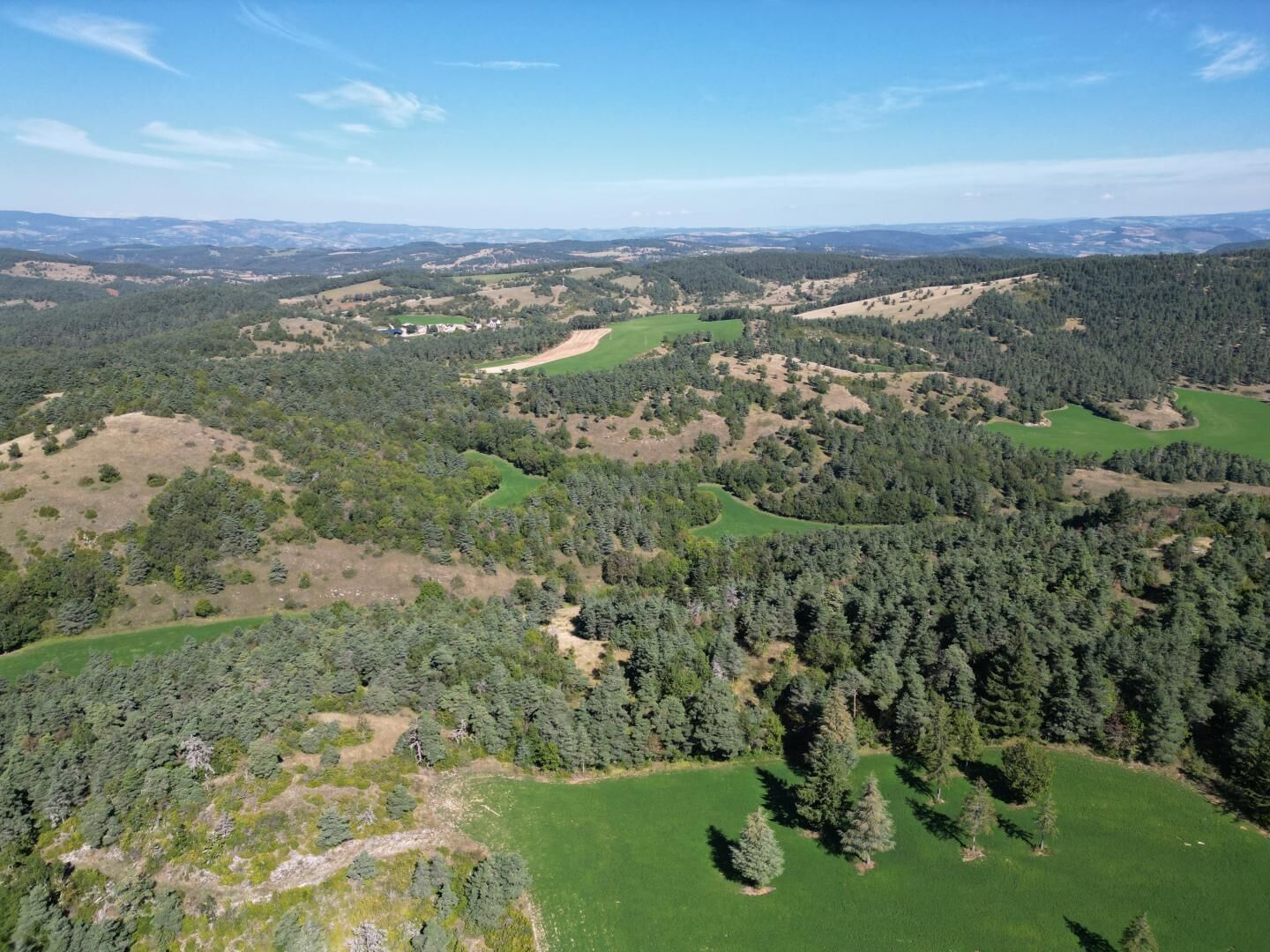 An aerial view of a rural landscape with dense forests, open fields, and rolling hills.