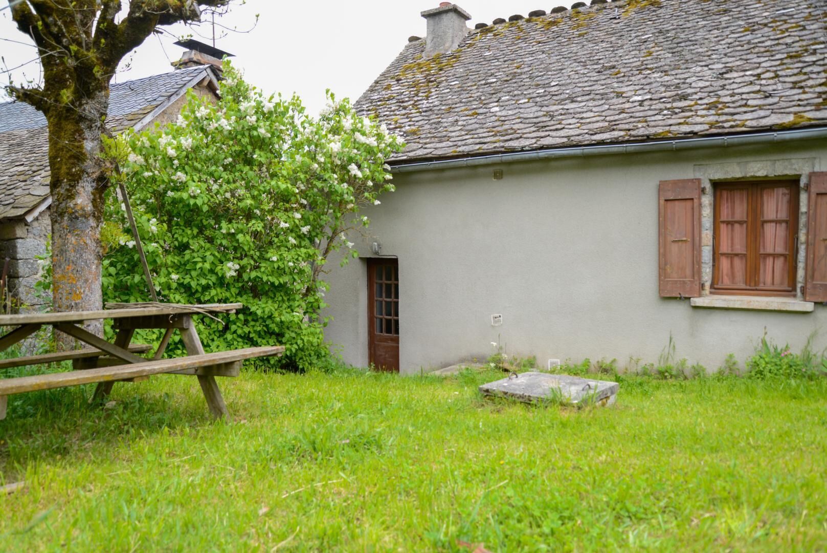 Un bâtiment rustique avec un toit en pierre, un banc en bois et un petit jardin.