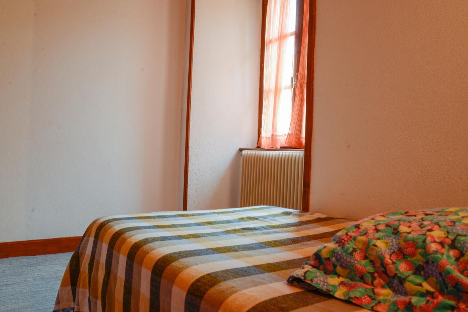 Een slaapkamer met een bed, een radiator en een raam met gordijnen.