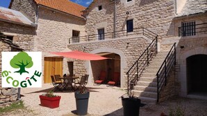 A stone building with a red-tiled roof, a staircase, and outdoor seating with a red umbrella.