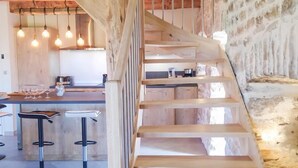 A wooden staircase leading to a kitchen area with hanging lights and a stone wall.