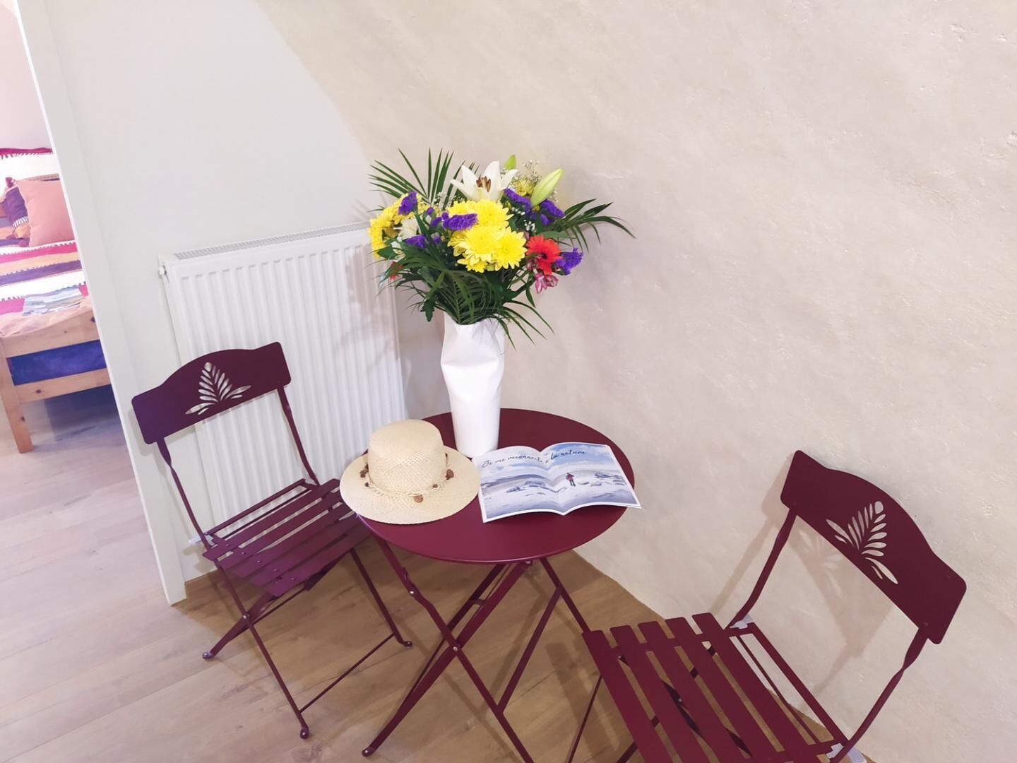 A small round table with a white vase of flowers, a straw hat, and an open book.